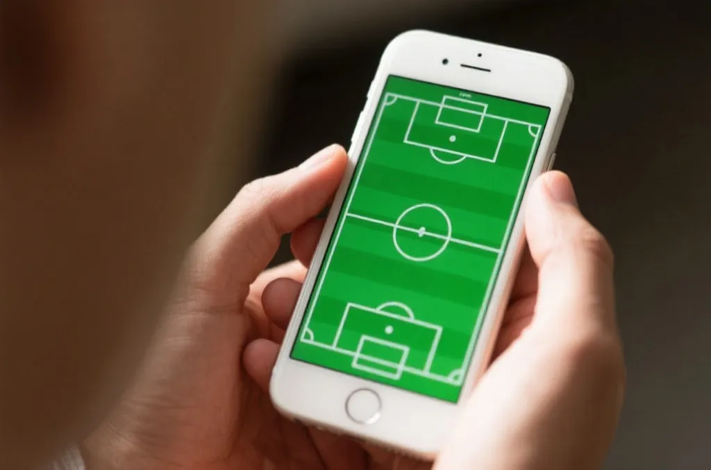 A close-up of a smartphone with a green soccer tactical board graphic, clean and professional look